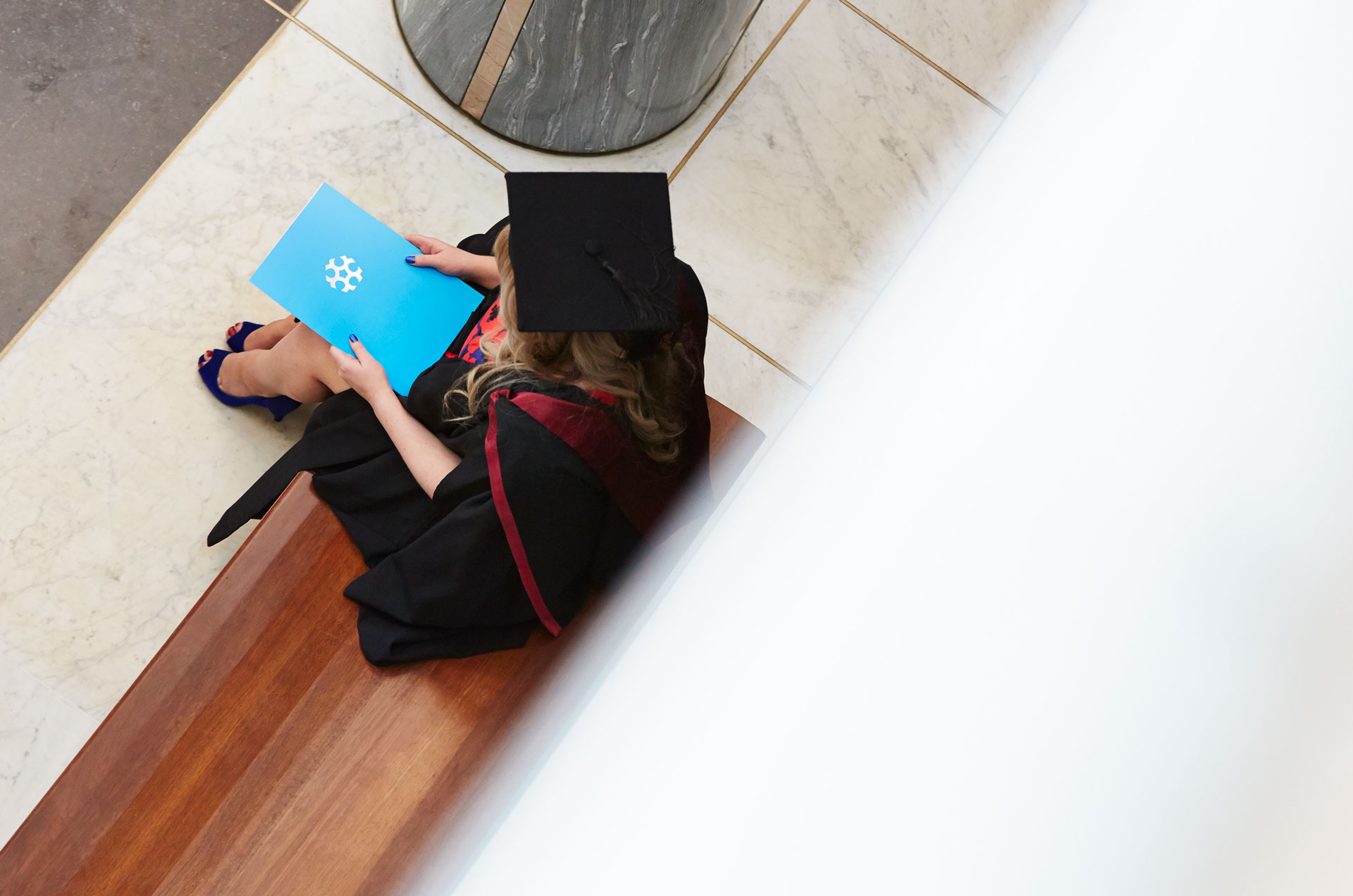 A graduate in a graduation gown sits with her University of Canberra folder